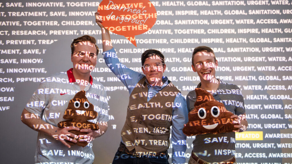 Three men standing together for a picture, holding poop emoji pillows and an orange speech bubble