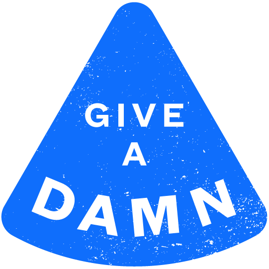 A blue triangle with the words "GIVE A DAMN" in black, with "DAMN" in bold, uppercase letters at the bottom. The shape and text have a slightly distressed texture.