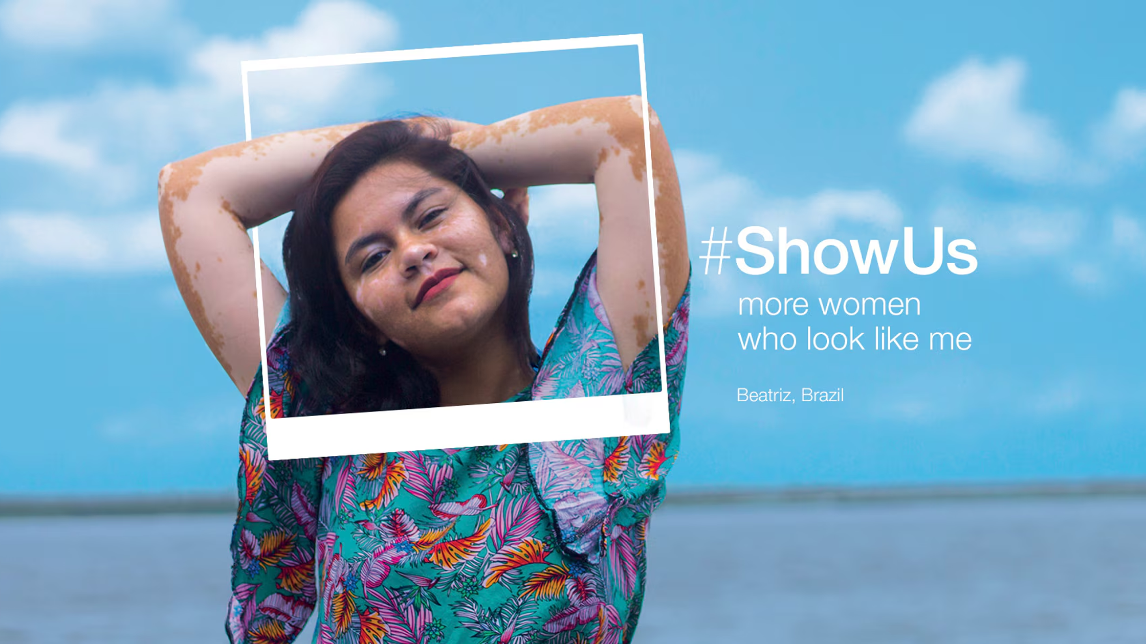 A woman stands outdoors, hands behind her head in a floral shirt. The sky and sea stretch beautifully behind her. The text reads "#ShowUs more women who look like me, Beatriz, Brazil." Discover real stories from real people who inspire through authentic design.