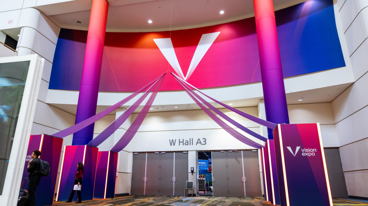 Entrance to W Hall A3 at a convention center, decorated with purple and pink fabric and columns, features a large "V" and "Vision Expo" signage—an inviting scene for attendees engaged in health advocacy and communication.