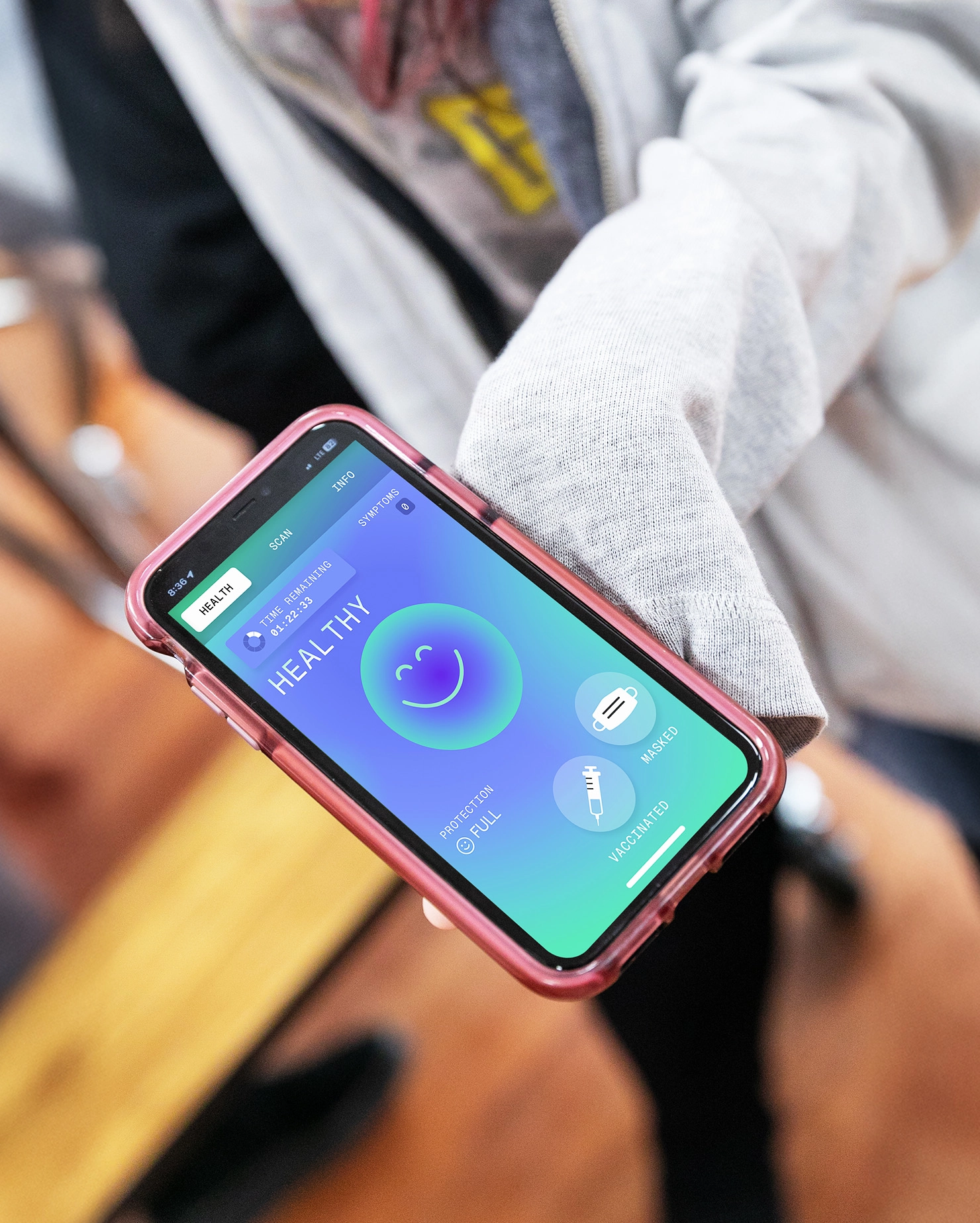 A person holds a smartphone displaying a health app with a smiling face and "HEALTHY" on the screen, showing vaccination status and health pass in a pink case—part of a global awareness campaign for public wellbeing.