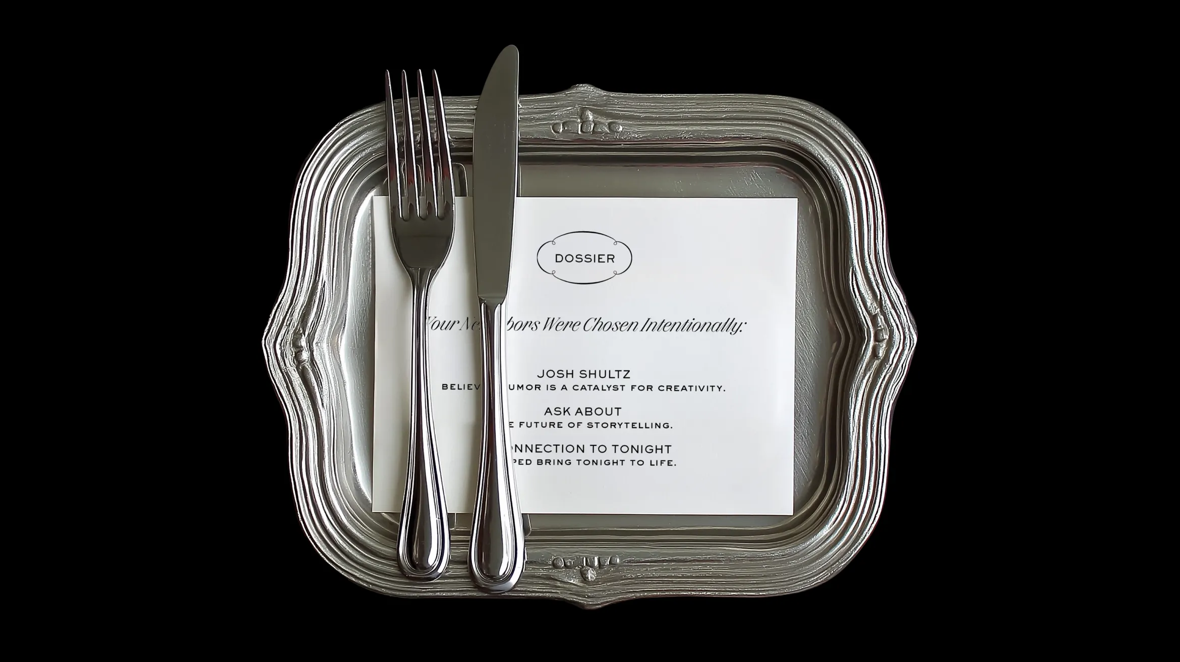 A silver fork and knife rest on a square, ornate silver plate with a printed card labeled “DOSSIER” underneath, all set against a black background.